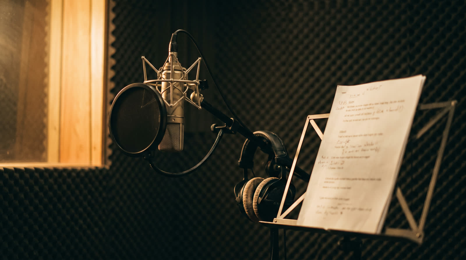 A studio microphone, headphones and a marked-up script in a recording booth